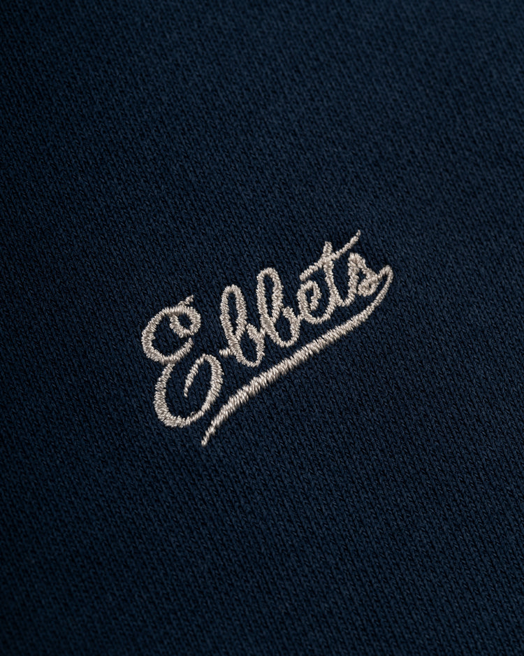 Close-up of the navy Ebbets Field Flannels Chest Logo Heavyweight Cotton Terry Crewneck, featuring Ebbets embroidered in white cursive on soft vintage-inspired fabric.