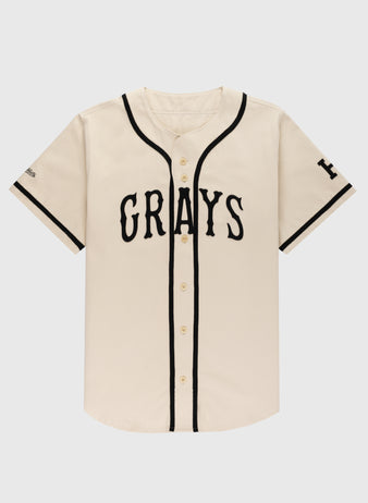 The Ebbets Field Flannels Homestead Grays Cotton Twill Baseball Jersey features a cream color, black piping, short sleeves with black trim, and bold “GRAYS” lettering across the chest in a classic button-up style.