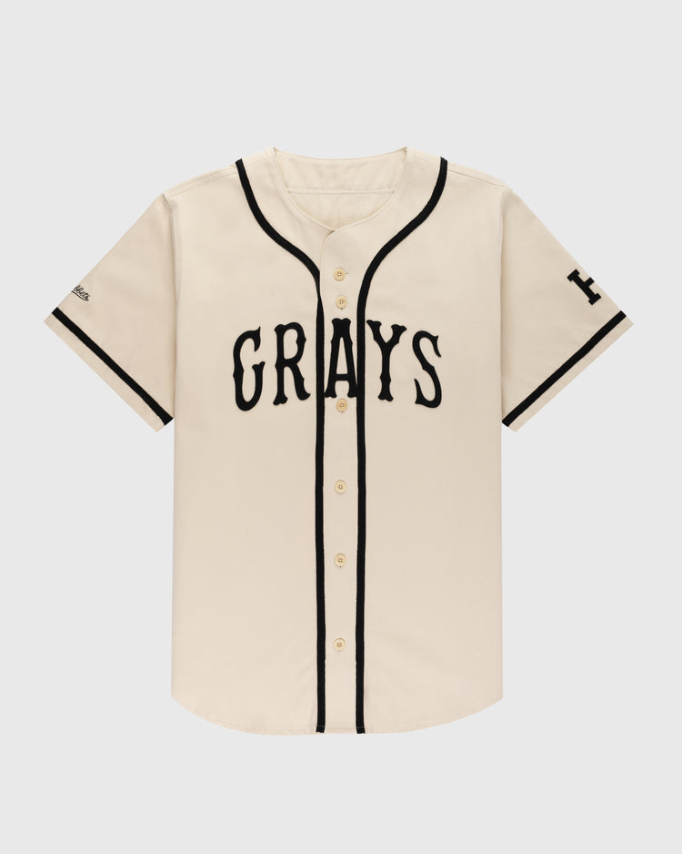 The Ebbets Field Flannels Homestead Grays Cotton Twill Baseball Jersey features a cream color, black piping, short sleeves with black trim, and bold “GRAYS” lettering across the chest in a classic button-up style.