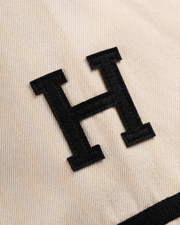 A close-up of a bold black H sewn onto beige cotton twill, echoing the vintage Homestead Grays style of the Ebbets Field Flannels Homestead Grays Cotton Twill Baseball Jersey.