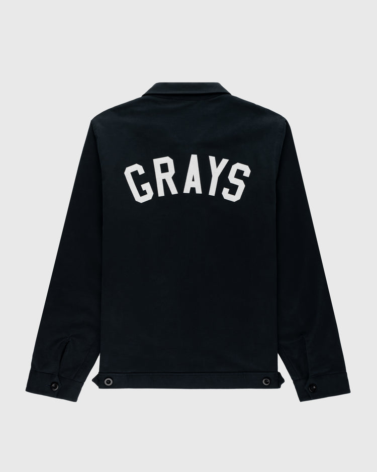 The Ebbets Field Flannels Homestead Grays Cotton Grounds Crew Jacket is a black cotton twill jacket featuring “GRAYS” in bold white letters across the upper back, inspired by the historic Homestead Grays, shown on a light gray background.