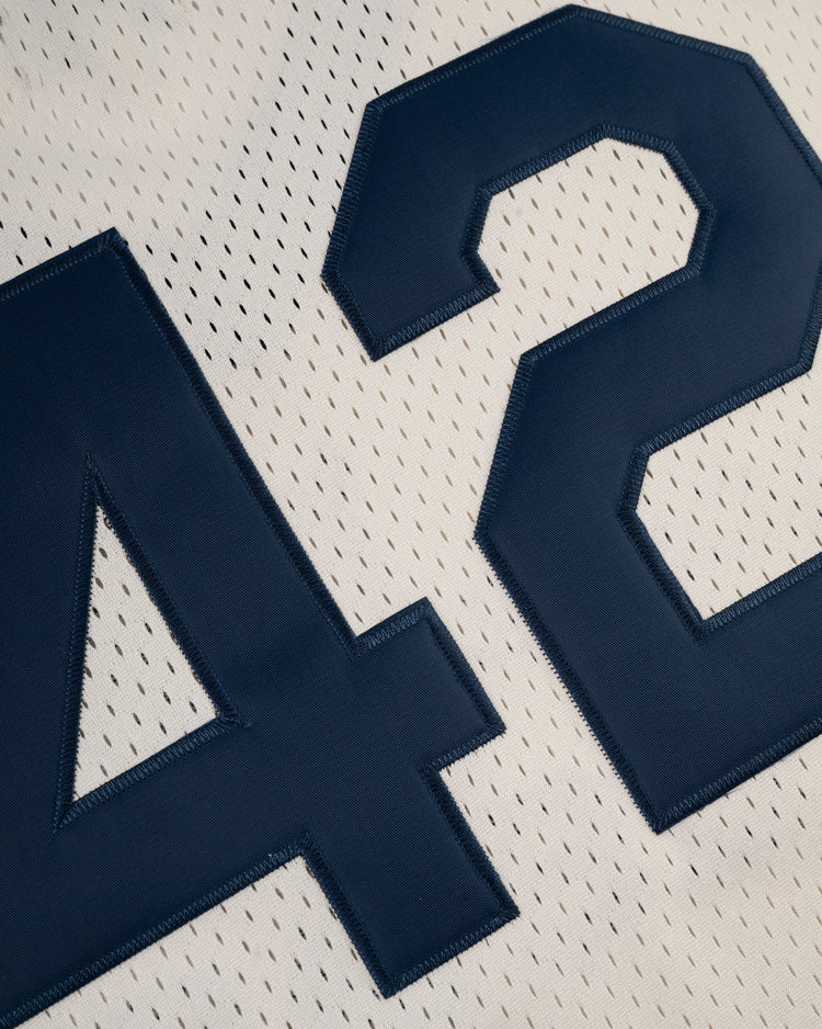 Close-up of the Ebbets Field Jackie Robinson Mesh V-Neck Jersey, featuring large navy 42s stitched on white mesh—perforated holes and vintage design honor the legendary baseball icon’s classic look.
