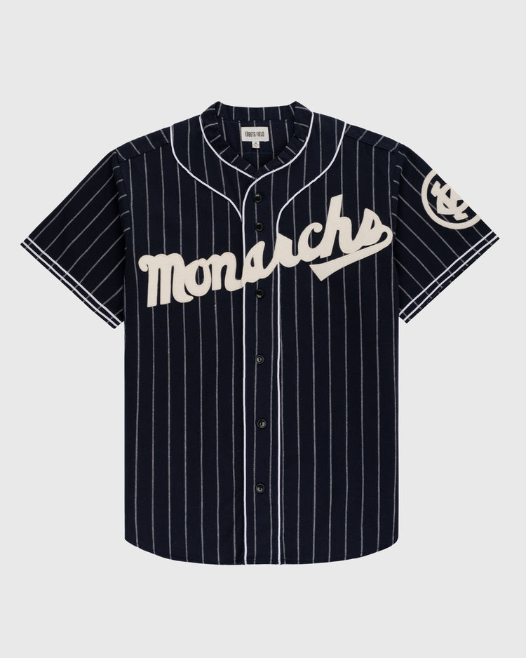 The Ebbets Field Kansas City Monarchs 1924 Authentic Wool Road Baseball Jersey features navy wool with white pinstripes, Monarchs script across the chest, and a classic Negro Leagues-inspired circular logo on the left sleeve.