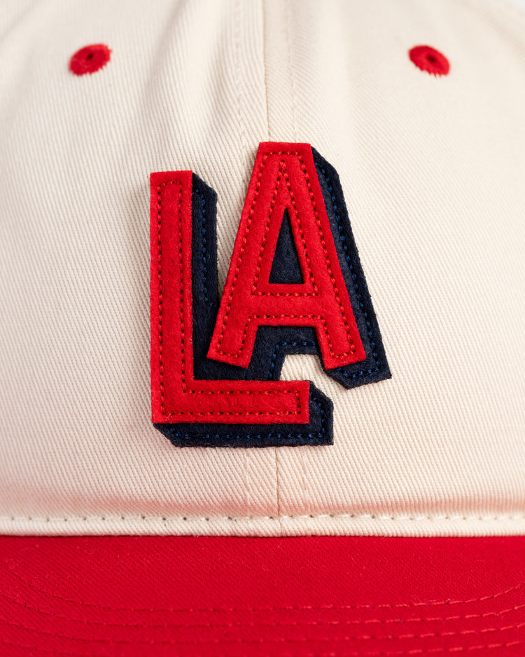 Close-up of the Los Angeles Angels (PCL) 1942 Logo Cotton Twill Ballcap by Ebbets Field—beige with a red brim and bold red LA letters outlined in black, perfect for vintage baseball hat collectors.