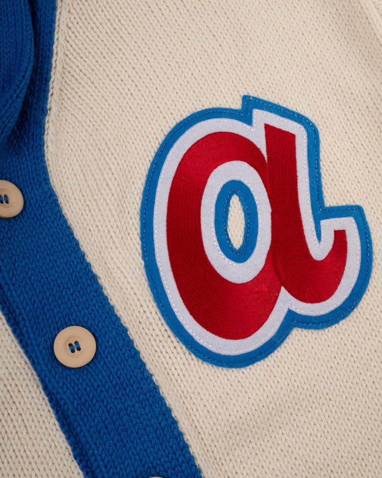 A close-up of the Atlanta Braves 1974 Wool Shawl Collar Sweater by Ebbets Field Flannels, cream-colored with blue trim and buttons, featuring a vintage-style red and white A patch outlined in blue.