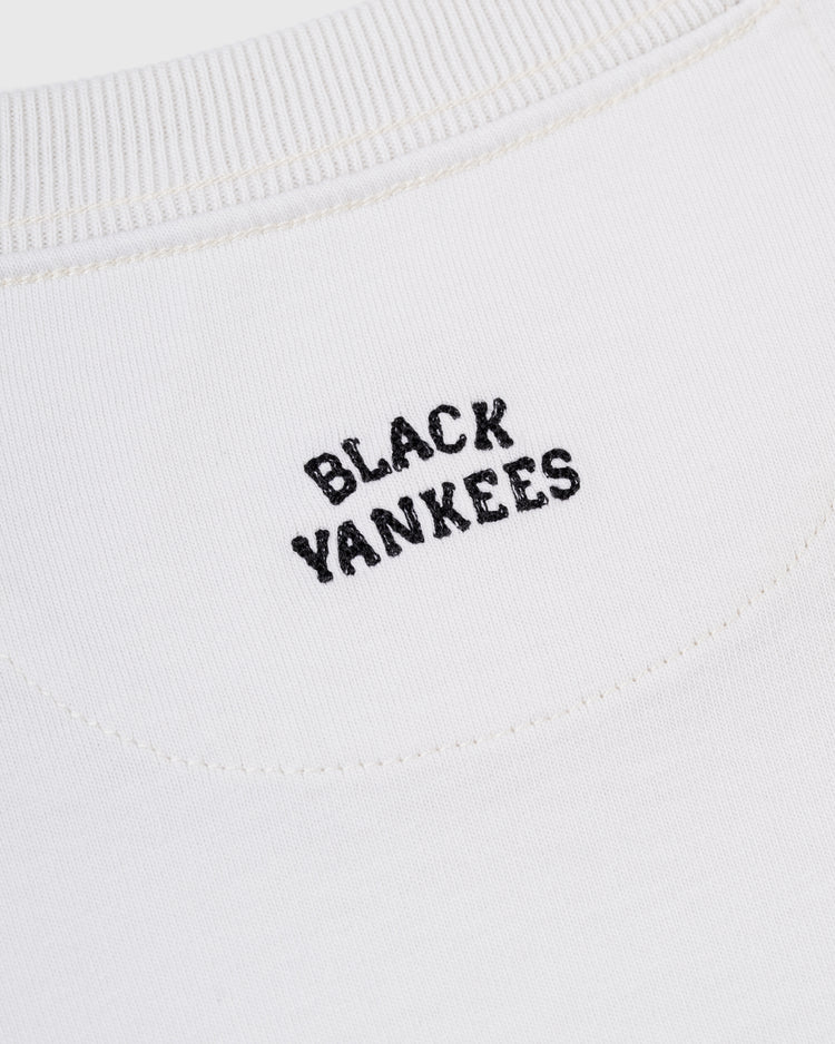 Close-up of the Ebbets Field New York Black Yankees Embroidered NY Short Sleeve Tee, featuring cream-colored fabric with BLACK YANKEES stitched in black near the neckline.