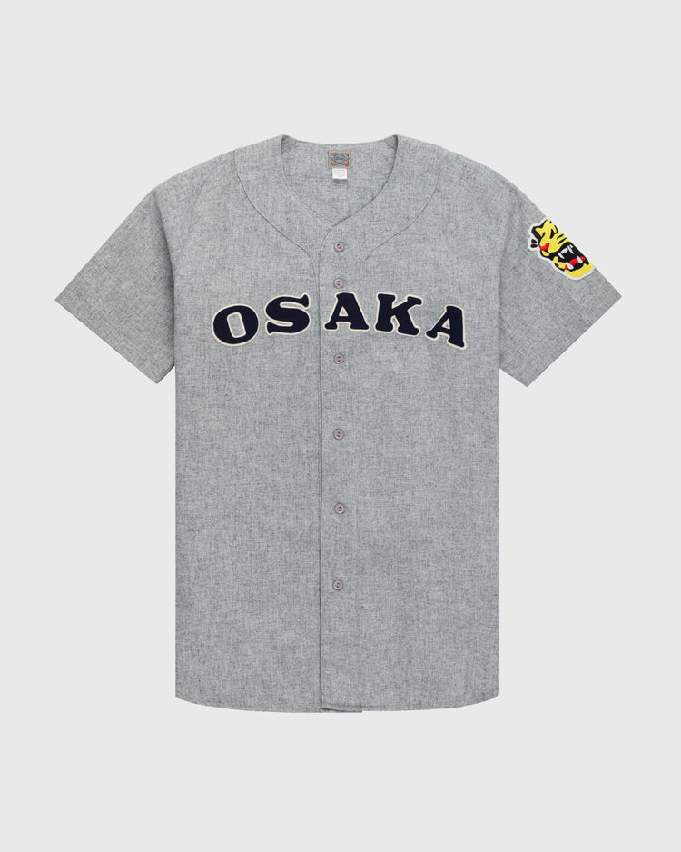 The Ebbets Field Flannels Osaka Tigers 1959 Authentic Wool Road Baseball Jersey features gray flannel, bold black OSAKA lettering, and a colorful tiger head patch on the sleeve, inspired by classic Koshien Field uniforms.