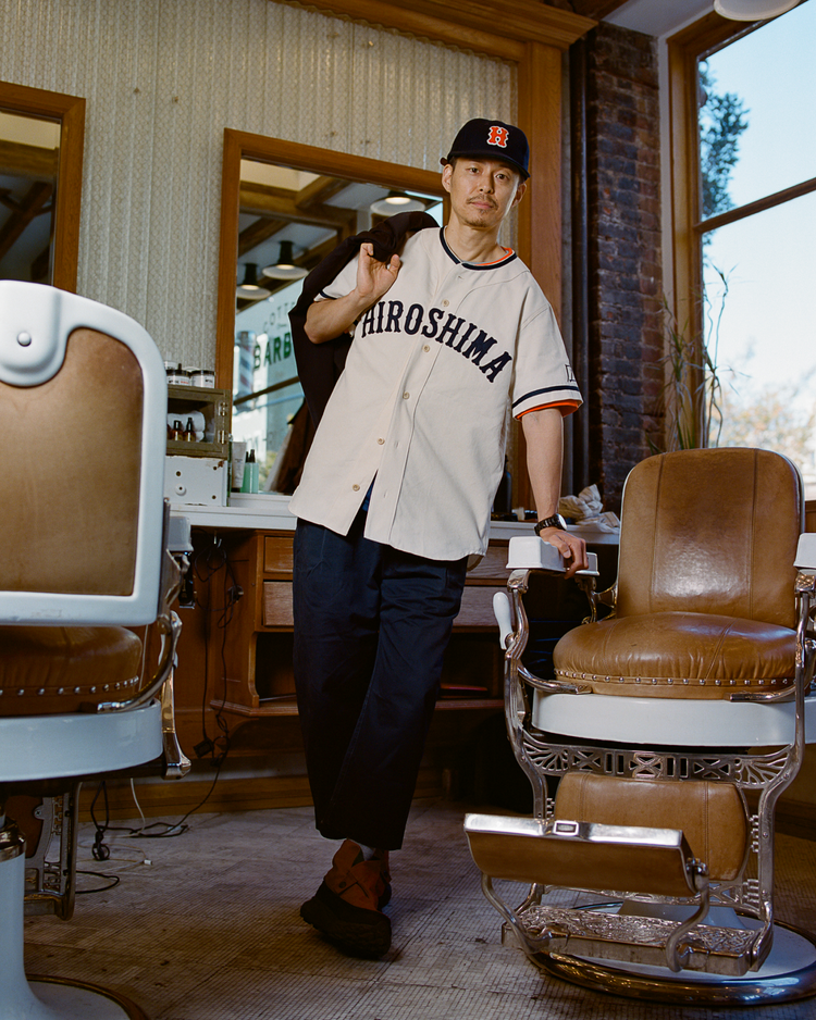 Man wearing a Hiroshima Carp baseball jersey in a barbershop.