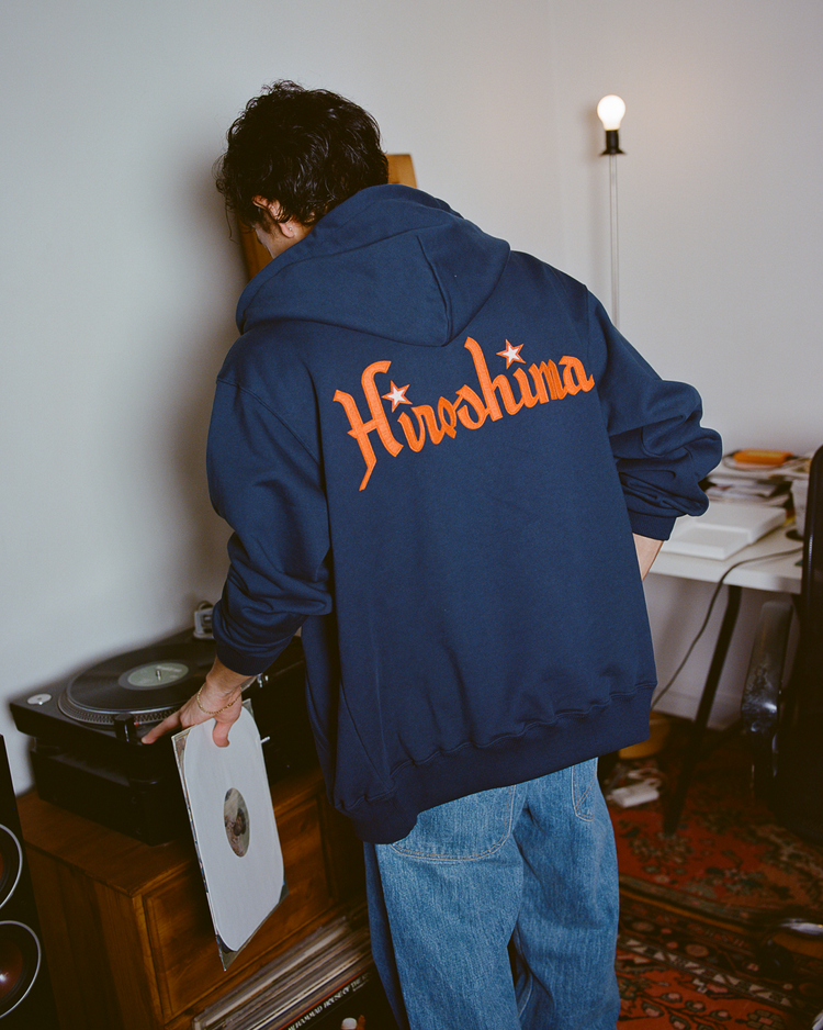 Person wearing a navy Hiroshima Carp hoodie with orange 'Hiroshima' text on the back, standing in a room with a record player.