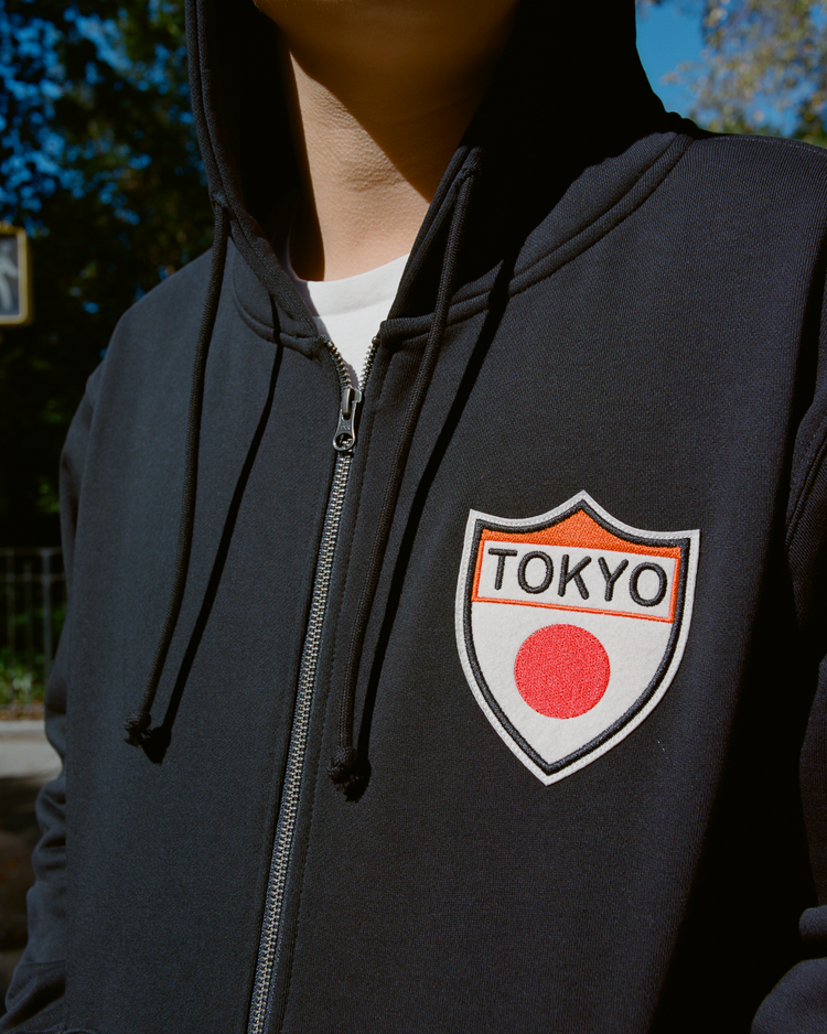 Person wearing a black Tokyo Giants' hoodie with a 'TOKYO' patch outdoors