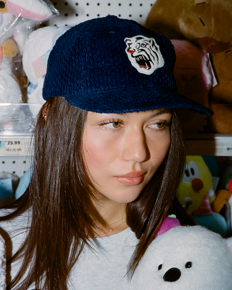 Person wearing an indigo corduroy cap with an Osaka Tigers logo, surrounded by stuffed animals and toys.