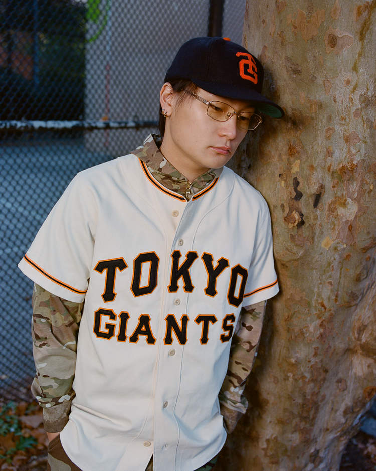 Person wearing a Tokyo Giants jersey and cap with an orange Tokyo Giants logo in an outdoor setting