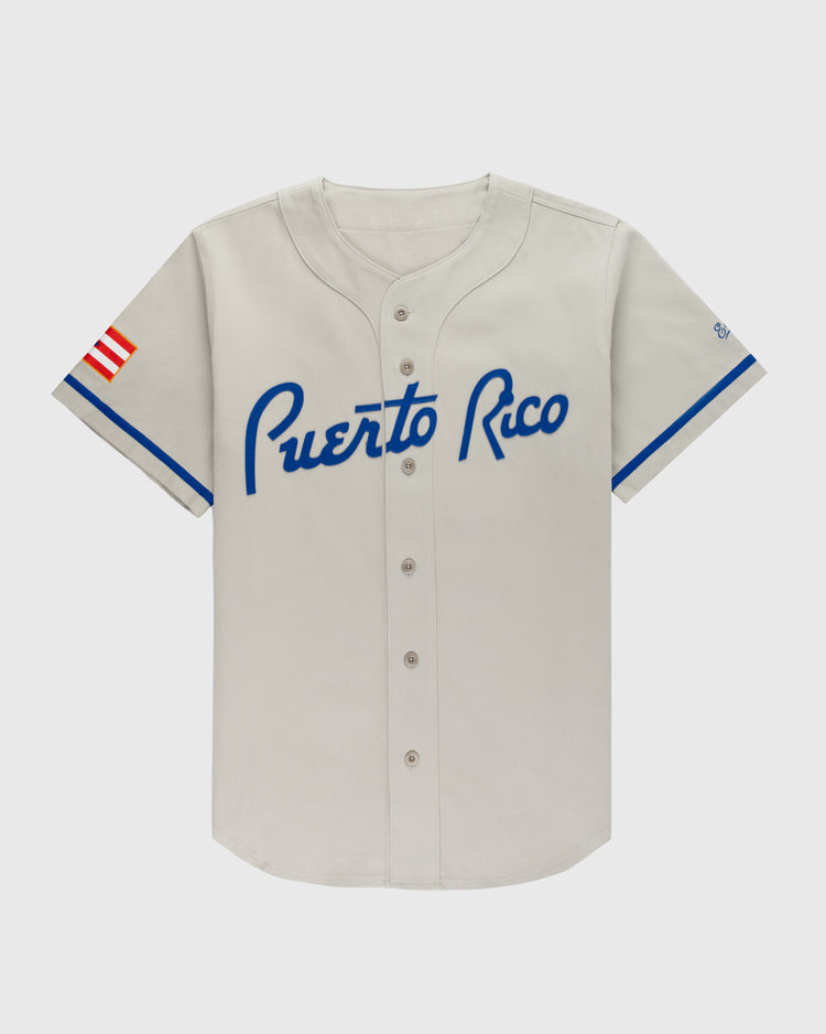 The Ebbets Field Puerto Rico 1958 National Team Cotton Twill Baseball Jersey is light gray with blue trim, “Puerto Rico” in blue script on the chest, and a red, white, and blue Puerto Rican flag patch on the left sleeve.