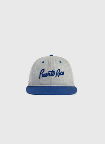 The Ebbets Field Puerto Rico 1958 National Team Cotton Twill Ballcap features a gray crown, blue brim, and Puerto Rico in blue script, inspired by the iconic Caribbean Series style. Shown against a simple light background.