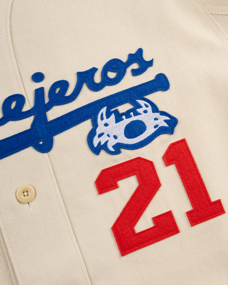 Close-up of the Ebbets Field Santurce Cangrejeros Cotton Twill Baseball Jersey, showcasing cream fabric, blue script, a wildcat logo, large red 21s, and a beige button—a nod to Puerto Ricos baseball legacy.
