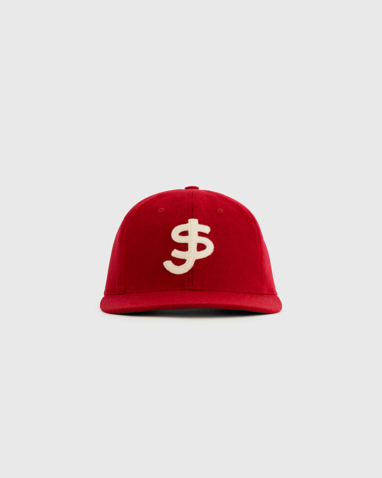 The Ebbets Field Flannels San Juan Senadores 1947 Authentic Wool Ballcap is a red replica hat with a bold white dollar sign on the front, inspired by the Puerto Rican League team and shown against a plain light gray background.