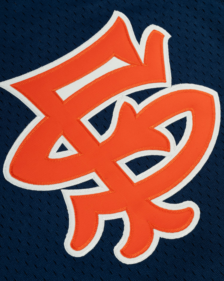 A close-up of the orange San Francisco Seals symbol with a white outline on dark blue textured polyester mesh, featured on the EFF San Francisco Seals Mesh V-Neck Jersey, reminiscent of vintage baseball style.