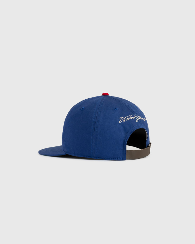 The Ebbets Field Santurce Cangrejeros Cotton Twill Ballcap features a blue crown, red top button, brown adjustable strap, and white cursive back embroidery inspired by Puerto Rican baseball, displayed against a plain gray background.