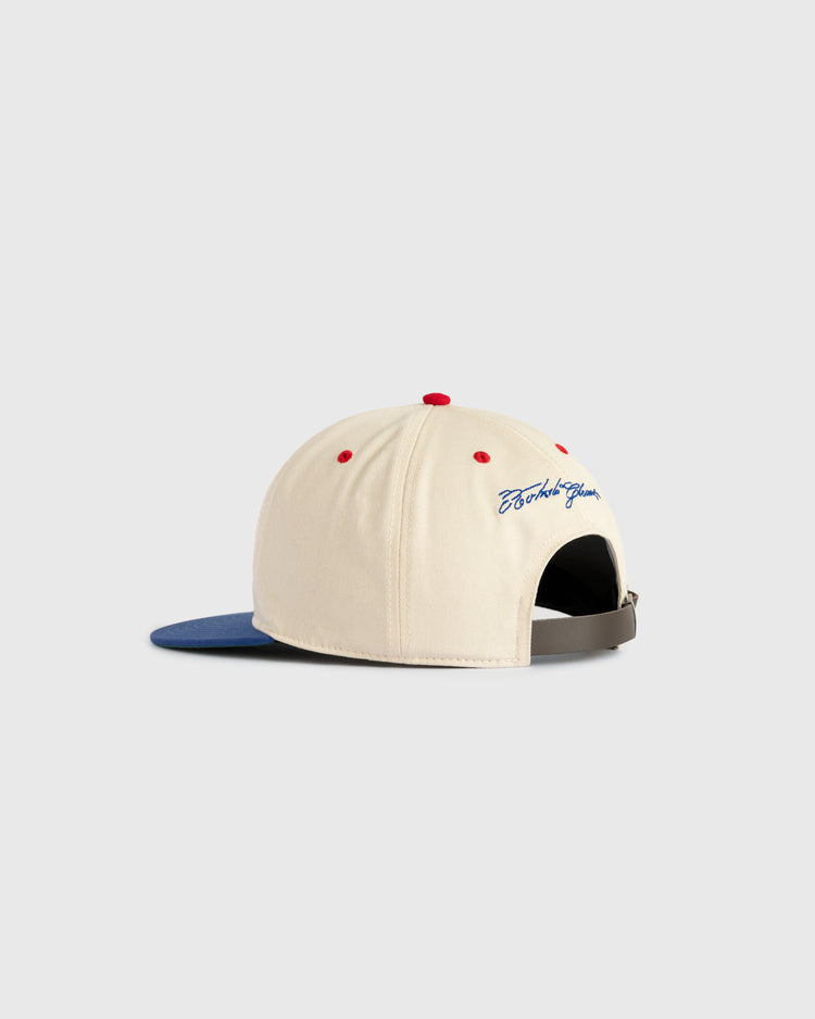 The Ebbets Field Santurce Cangrejeros Cotton Twill Ballcap features a cream crown, blue brim, red accents, adjustable strap, and blue cursive embroidery above the back opening. Shown on a light gray background.