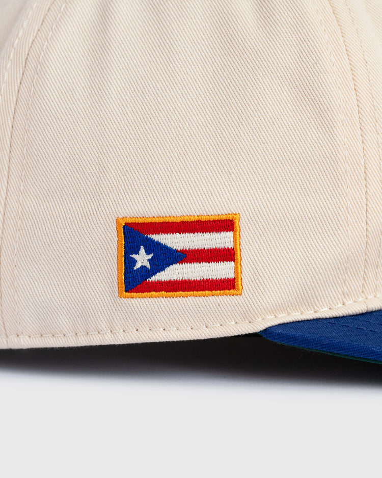 A close-up of the Ebbets Field Santurce Cangrejeros Cotton Twill Ballcap highlights an embroidered Puerto Rican flag on the front and features a green and blue brim, showcasing Puerto Rican baseball heritage.
