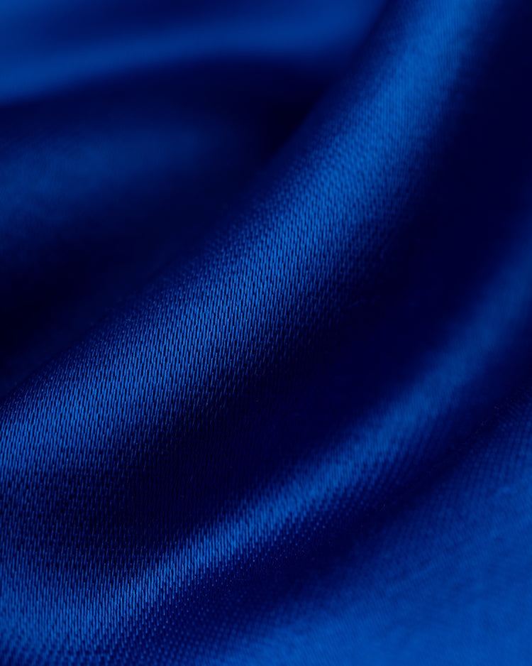 Close-up of smooth, flowing royal blue fabric with soft folds and a satin sheen, reflecting the silky texture and rich color of the EFF Seattle Mariners 1982 Satin Windbreaker Jacket.