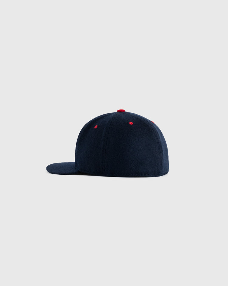 The EFF Seattle Rainiers 1957 Authentic Wool Ballcap is shown from the side in navy blue, featuring red-stitched eyelets and a red top button, faithfully recreating the 1957 style against a plain light gray background.
