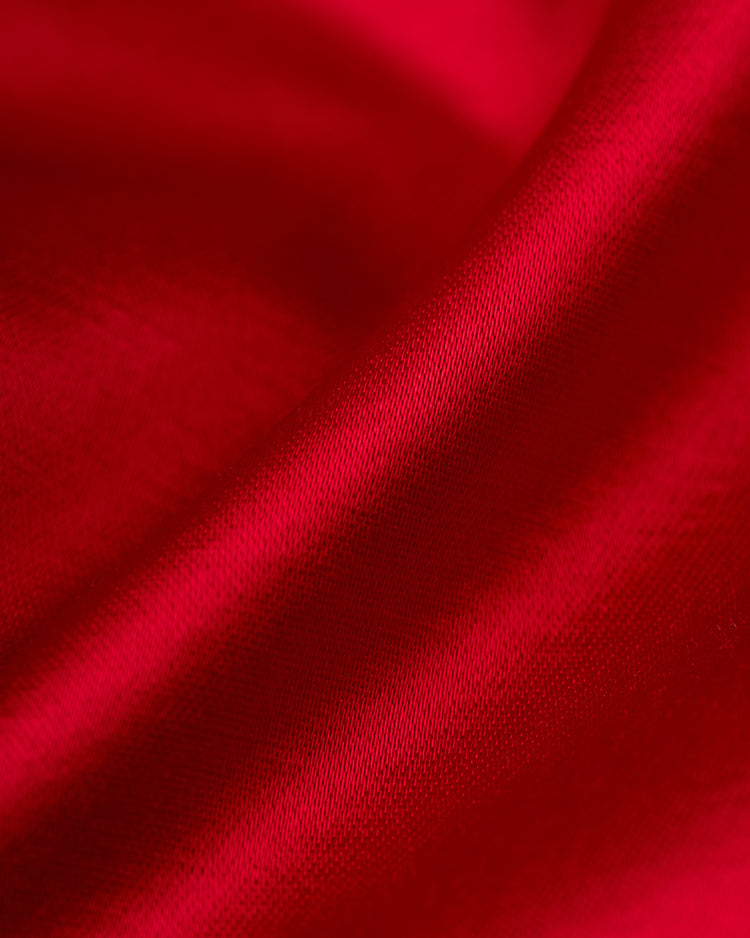 Close-up of smooth, shiny red fabric with soft folds and highlights, capturing the luxurious elegance of the EFF Cincinnati Reds 1955 Satin Windbreaker Jacket.