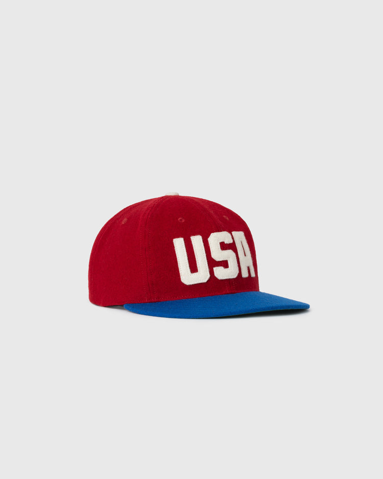 The EFF USA National Team 1956 Authentic Wool Ballcap features a red crown, blue brim, and bold white “USA” letters on the front, shown against a plain light gray background.