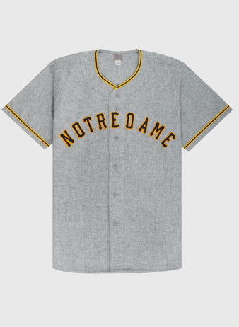 The Ebbets Field University of Notre Dame 1956 Authentic Wool Road Baseball Jersey features gray wool, gold and black NOTRE DAME lettering, and matching trim, inspired by the classic 1956 road uniform.