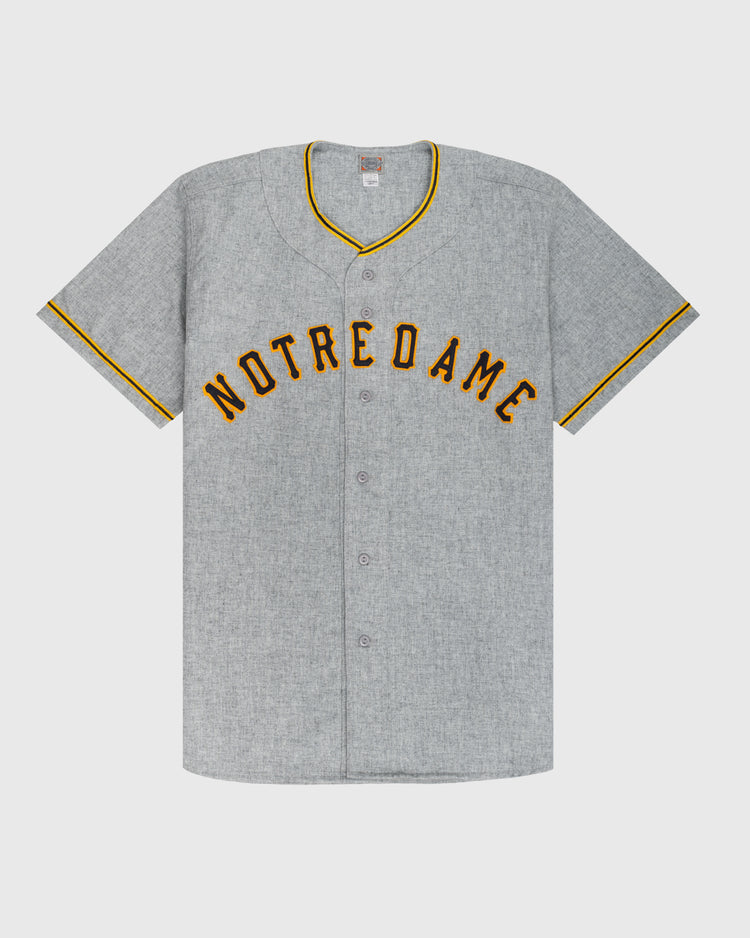 The Ebbets Field University of Notre Dame 1956 Authentic Wool Road Baseball Jersey features gray wool, gold and black NOTRE DAME lettering, and matching trim, inspired by the classic 1956 road uniform.