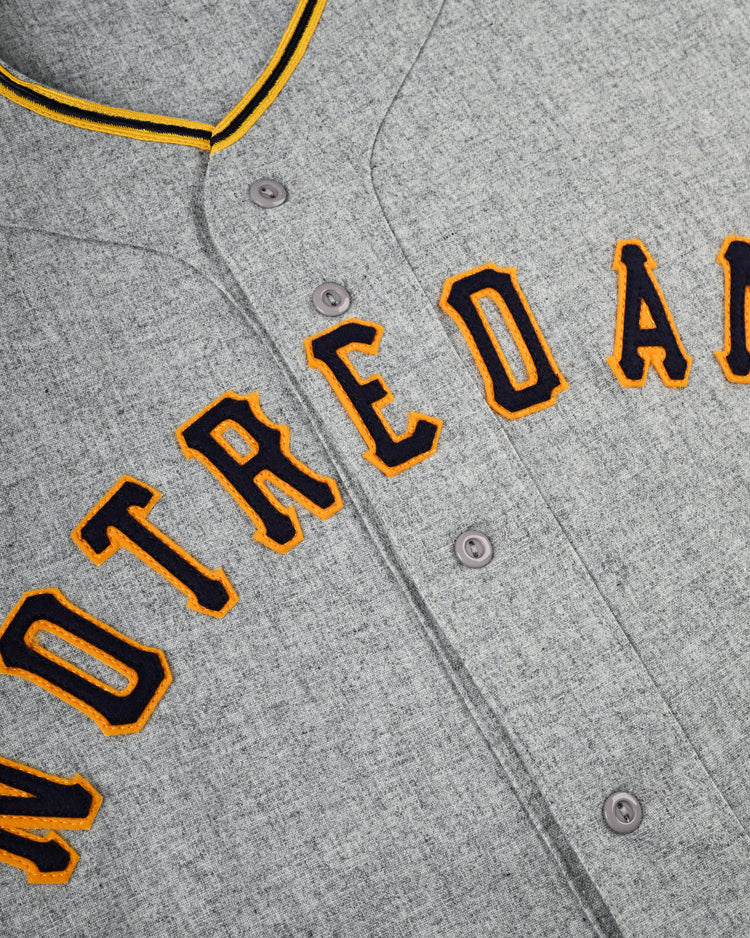 A close-up of the Ebbets Field University of Notre Dame 1956 Authentic Wool Road Baseball Jersey, featuring NOTRE DA in large gold and black outlined letters across the chest and yellow-trimmed collar for classic Fighting Irish style.