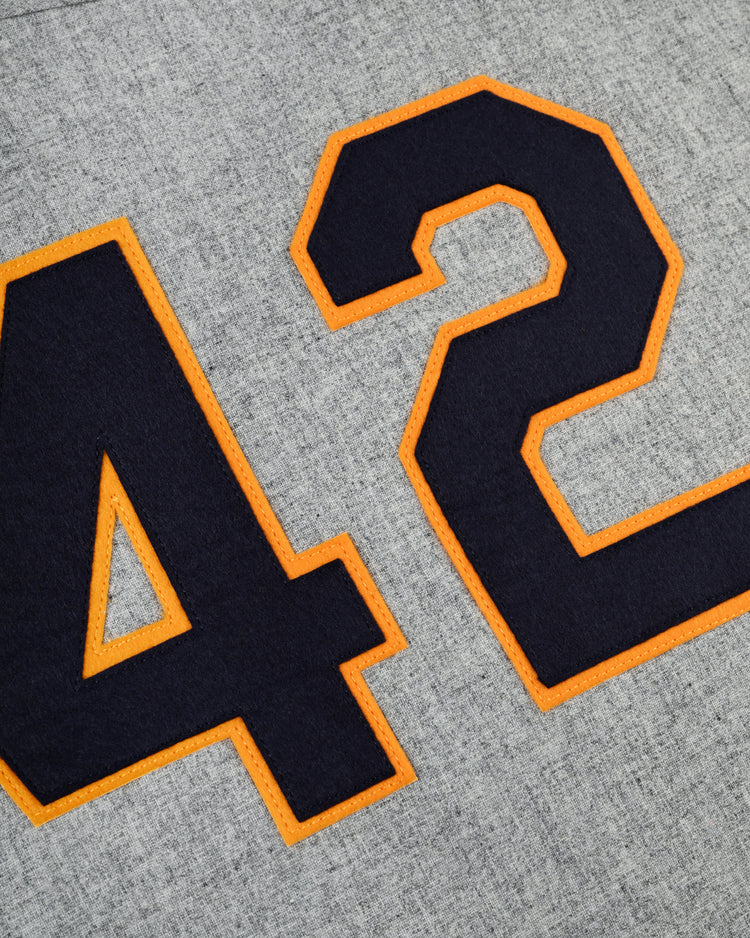 A close-up of the number 42 in dark blue with orange outlines, sewn on gray wool—detail from the Ebbets Field University of Notre Dame 1956 Authentic Road Baseball Jersey.