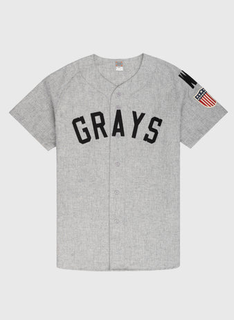 The Ebbets Field Flannels Homestead Grays 1944 Authentic Wool Road Baseball Jersey features short sleeves, GRAYS in black on the front, a U.S. flag patch on the left sleeve, and is crafted from authentic wool flannel for true vintage feel.