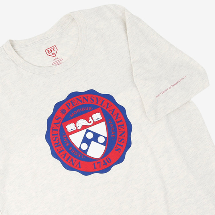 The EFF University of Pennsylvania T-Shirt in natural features the Penn crest in red and blue, with Universitas Pennsylvaniensis 1740 encircling it, inspired by legendary football star and NFL Draft pick Chuck Bednarik.
