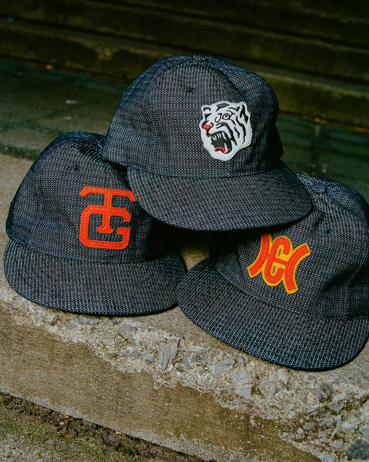 Three Hiroshima Carp Japanese Indigo Cotton Dobby Ballcaps by Ebbets Field, each with a unique embroidered design, are displayed outdoors on rugged concrete steps.