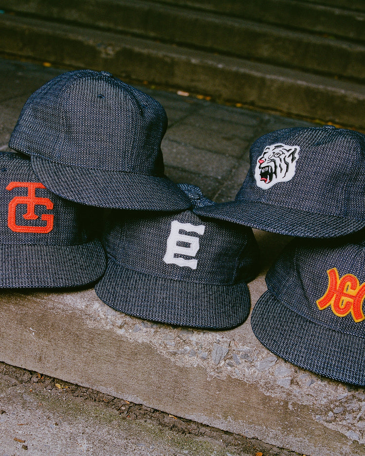 Five dark-colored baseball caps, including the Ebbets Field Tokyo Giants 1940 Japanese Indigo Cotton Ballcap, are displayed on a concrete ledge outdoors with stone steps in the background.