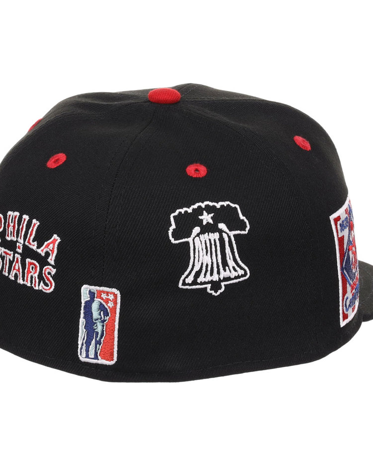The Ebbets Field Philadelphia Stars NLB Varsity Fitted Ballcap is black with red and white embroidered PHILA STARS, a Liberty Bell, and a basketball player. Red accents highlight the button and ventilation holes.