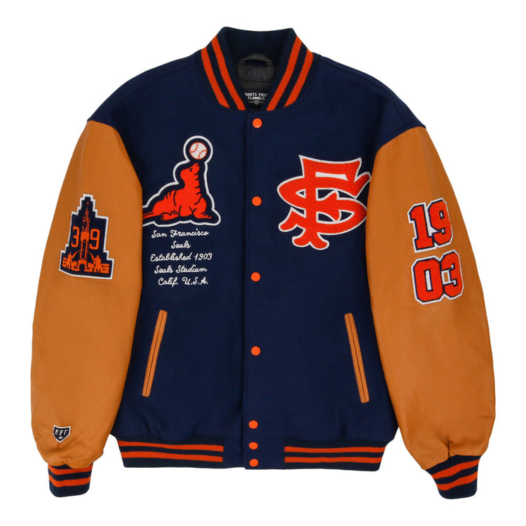 The Ebbets Field San Francisco Seals MiLB Dna Varsity Jacket features navy and tan colors with orange accents, chest patches like SF, 1903, a baseball graphic, San Francisco Seals text, and city/team details on the sleeves.