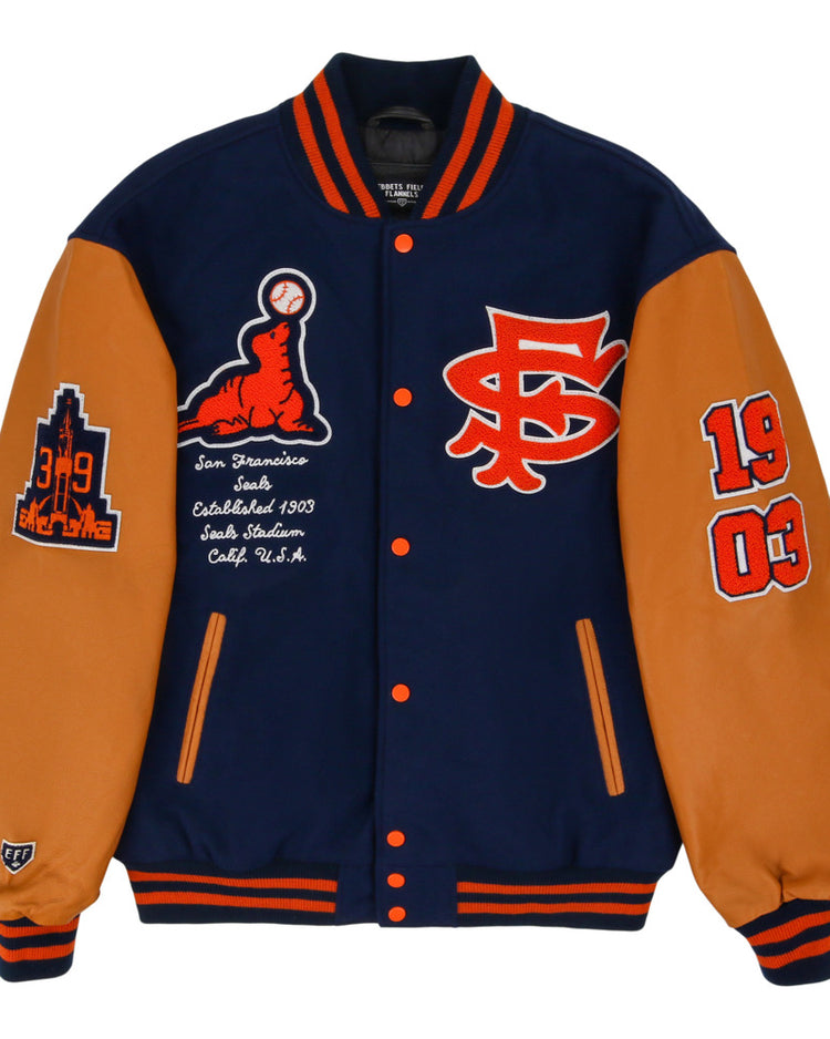 The Ebbets Field San Francisco Seals MiLB Dna Varsity Jacket features navy and tan colors with orange accents, chest patches like SF, 1903, a baseball graphic, San Francisco Seals text, and city/team details on the sleeves.