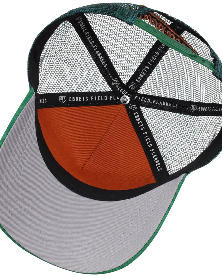 The inside view of the Greensboro Grasshoppers MiLB Trucker Ballcap by Ebbets Field shows green, gray, and orange mesh panels, an orange sweatband, and black straps labeled “EBBETS FIELD FLANNELS.”.