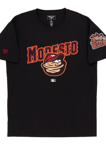 The Ebbets Field Modesto Nuts MiLB Fashion Cotton Short Sleeve Tee features a cartoon nut character, bold red MODESTO lettering, a chest logo, and a Nuts logo patch on the left sleeve.