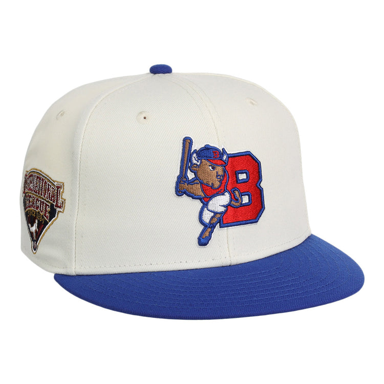 The Ebbets Field Buffalo Bisons MiLB Snapback Ballcap is a white cap with a blue brim, featuring a cartoon buffalo swinging a bat by a red 