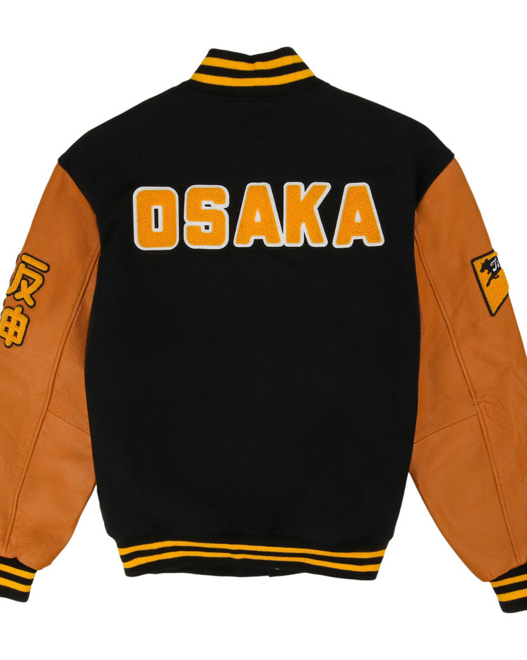 The Osaka Tigers DNA Varsity Jacket by Ebbets Field features a black and brown design, OSAKA in bold yellow and white on the back, yellow-striped cuffs/collar, and sleeve patches with Japanese characters.