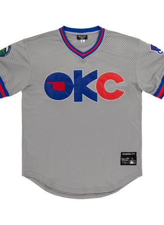 The Ebbets Field Oklahoma City 89Ers MiLB V-Neck Jersey features gray mesh with blue and red trim, OKC in bold on the front with an Oklahoma state silhouette inside the O, sleeve patches, and a stitched label near the hem.