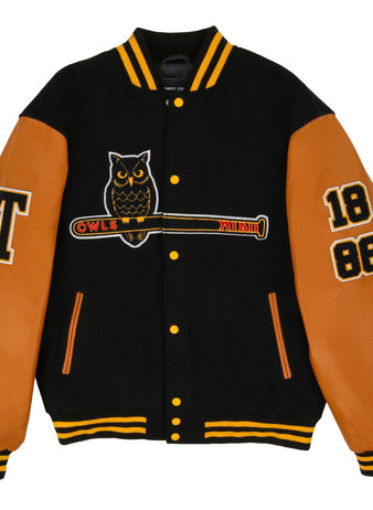 The Ebbets Field Topeka Owls MiLB Dna Varsity Jacket is black with tan leather sleeves, features an owl-on-bat patch, OWLS text, 1886 on the right sleeve, a large T on the left sleeve, and yellow striped collar and cuffs.