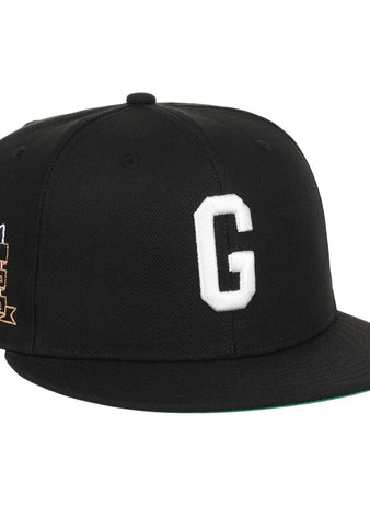 The Ebbets Field Homestead Grays NLB Tc Fitted Ballcap is a black cap with a white embroidered “G” on the front and a colorful patch featuring text and stars on the left side.