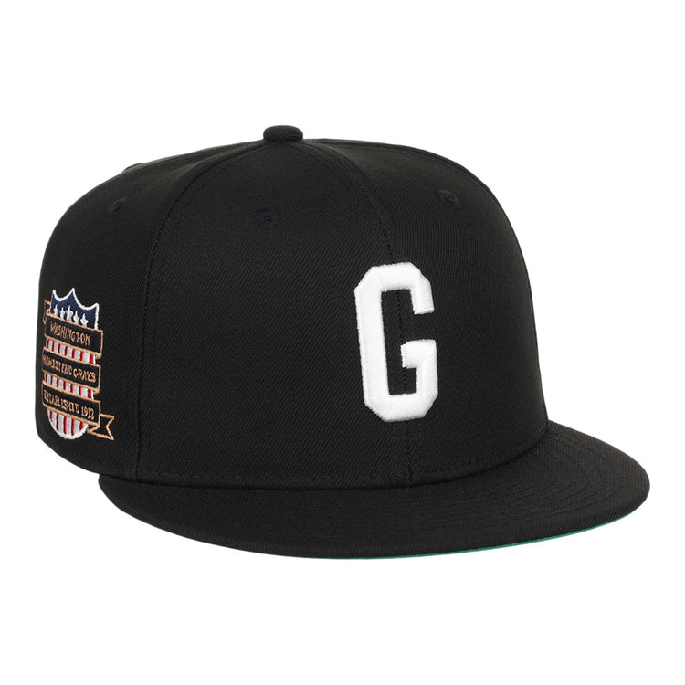 The Ebbets Field Homestead Grays NLB Tc Fitted Ballcap is a black cap with a white embroidered “G” on the front and a colorful patch featuring text and stars on the left side.