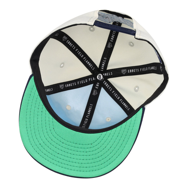 The image shows the inside of the Columbus Clippers MiLB Snapback Ballcap by Ebbets Field, featuring an off-white crown with black Ebbets Field taping and a light green underside on the brim with black stitching.