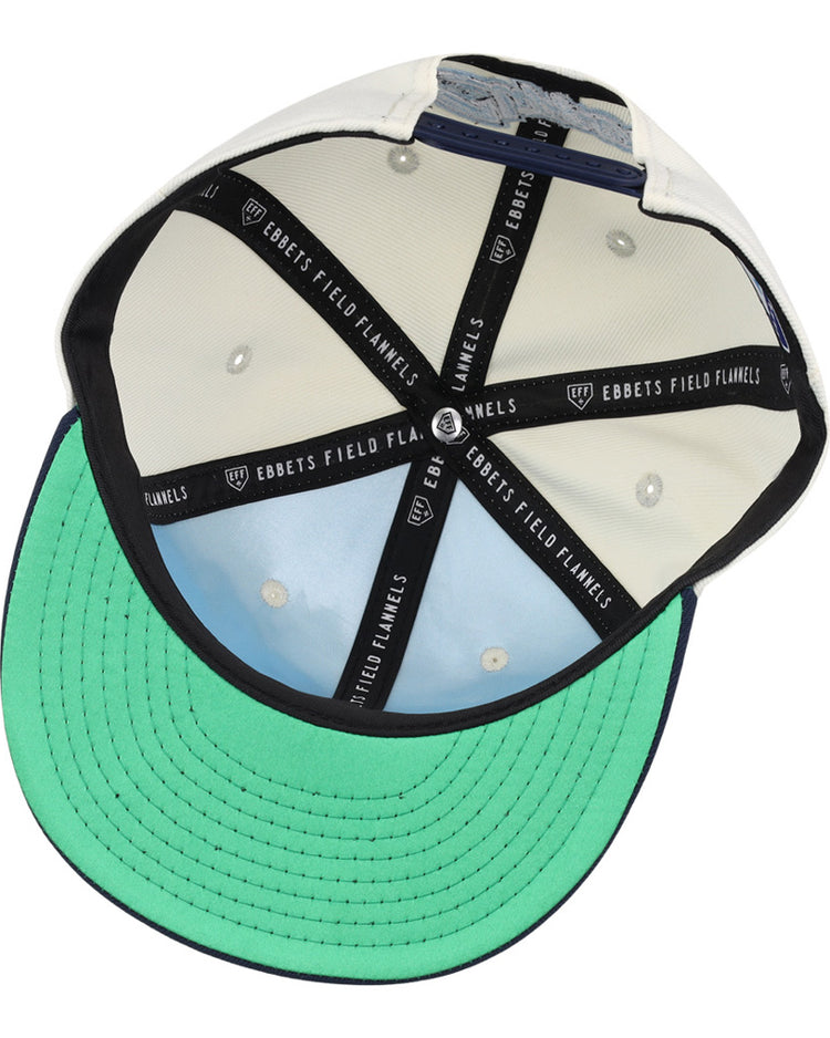 The image shows the inside of the Columbus Clippers MiLB Snapback Ballcap by Ebbets Field, featuring an off-white crown with black Ebbets Field taping and a light green underside on the brim with black stitching.