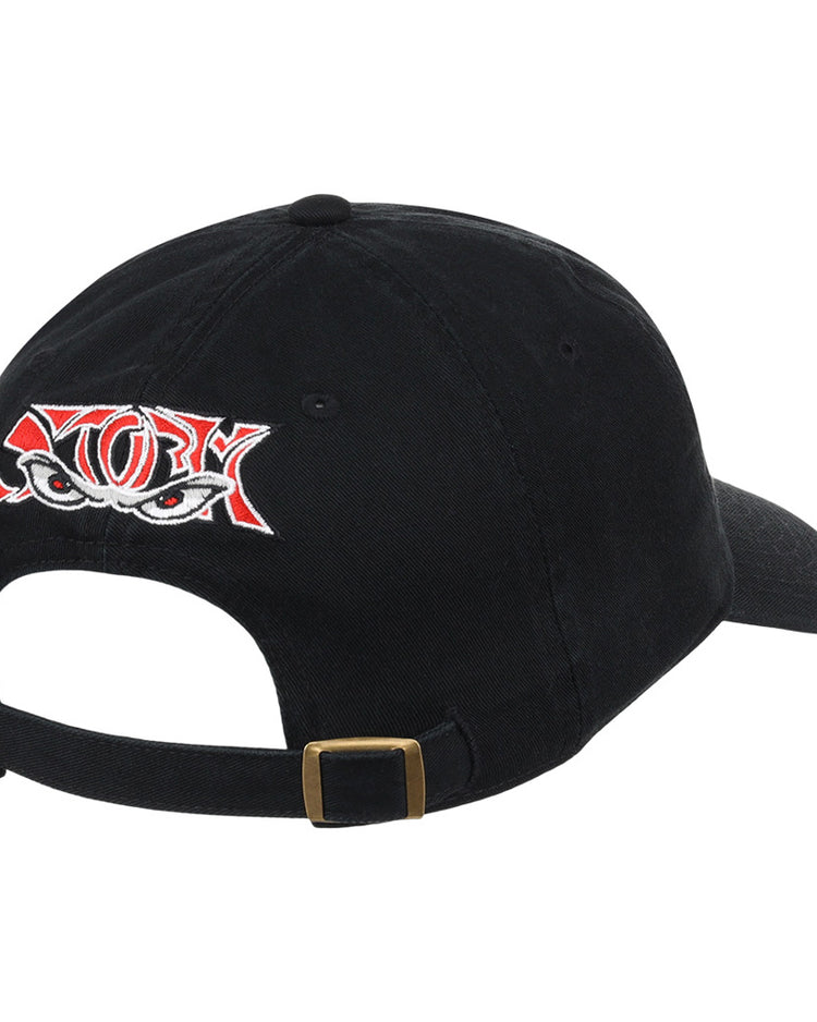 The Ebbets Field Lake Elsinore Storm MiLB Dad Ballcap is a black cap featuring red and white embroidered eyes on the back, plus an adjustable strap with a brass buckle.